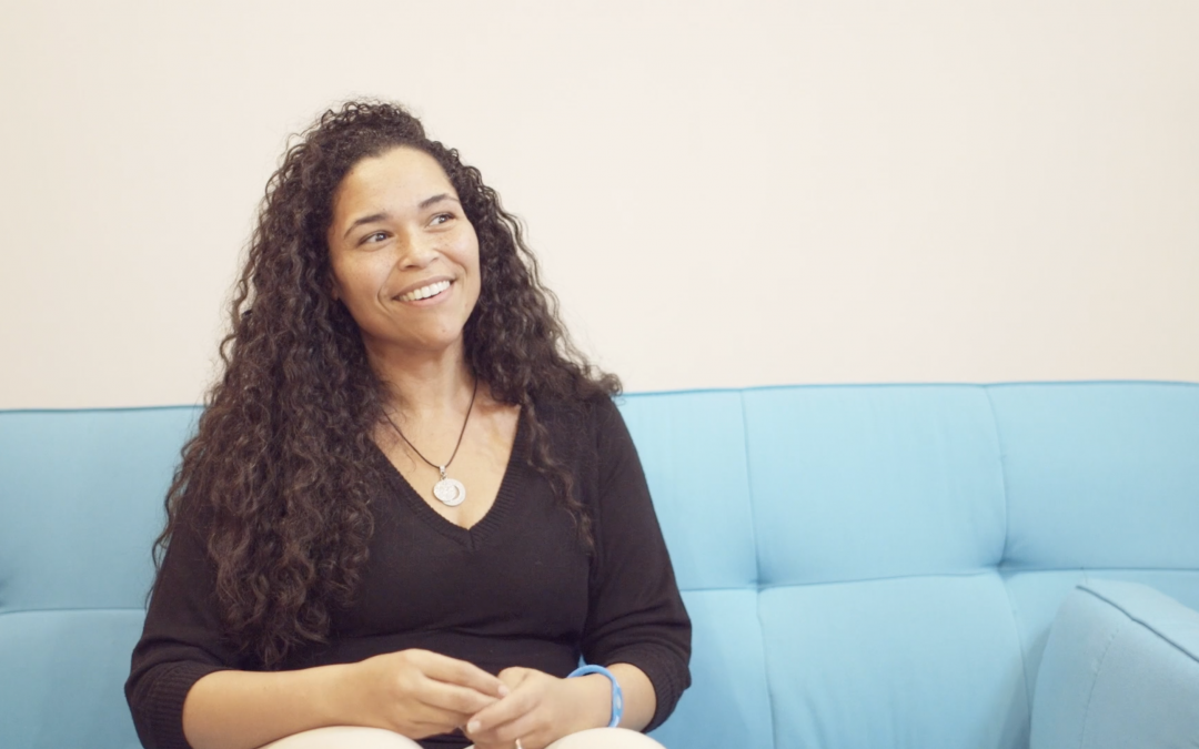 woman with curly hair sitting on blue couch giving testimonial
