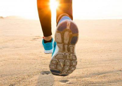 close up of woman's lower leg and blue sneakers while running on sand